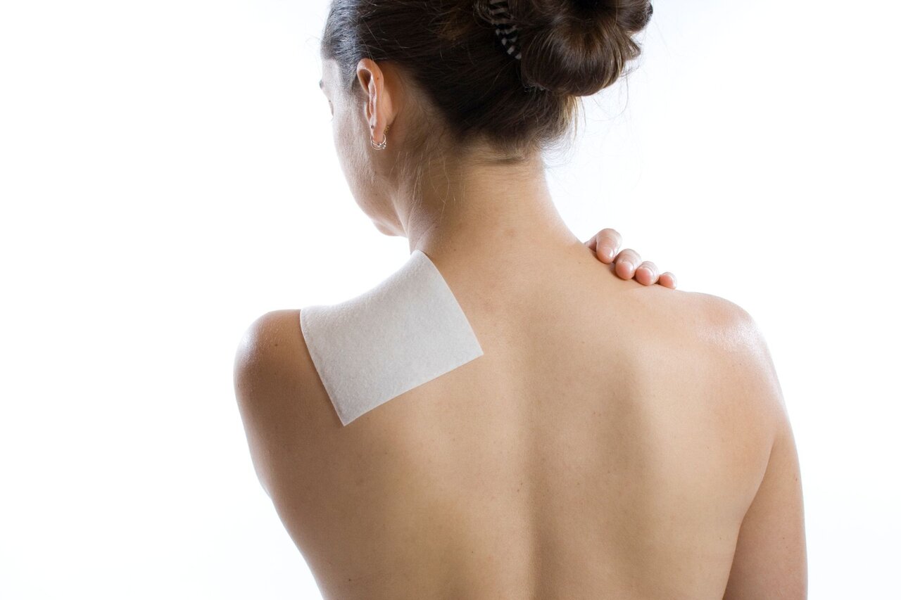 Frau mit Wärmepflaster auf der schmerzenden Schulter – Anwendung einer konservativen Therapie zur Linderung chronischer Schulterschmerzen.