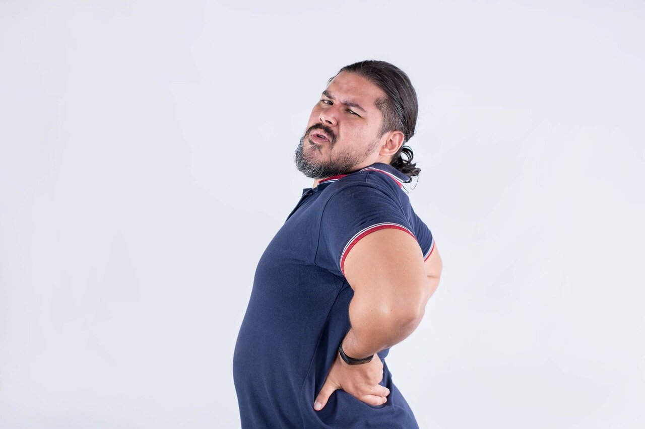 Mann mit schmerzverzerrtem Gesicht greift sich an den Rücken – Hinweis auf akuten Bandscheibenvorfall mit möglicher Ausstrahlung in den Rückenbereich.