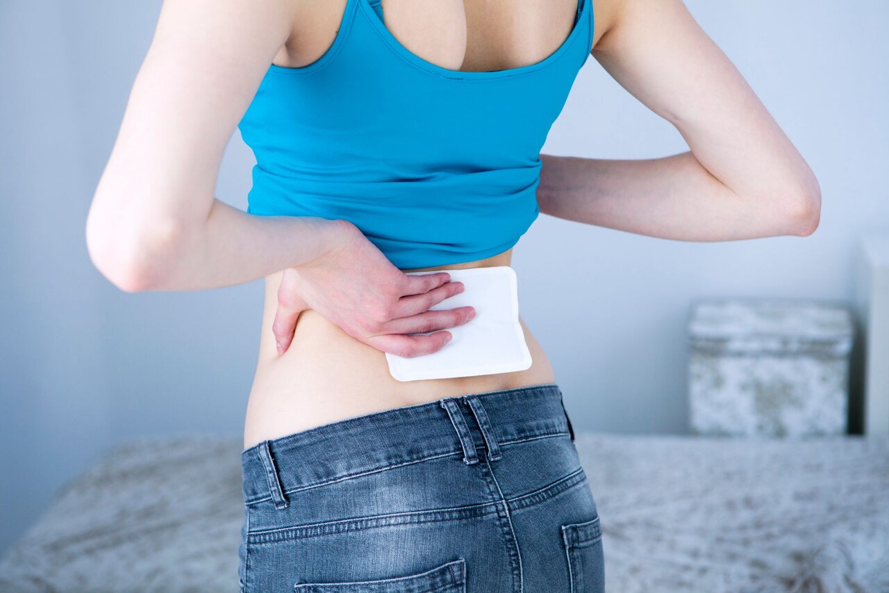 Frau mit Wärmepflaster im unteren Rückenbereich – typische Maßnahme zur Schmerzlinderung bei Verspannungen und Kreuzschmerzen.