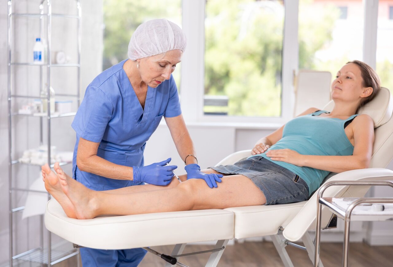 Medizinisches Fachpersonal führt eine Injektion in das Knie einer liegenden Patientin durch – Behandlung einer Schleimbeutelentzündung mittels Kortisonspritze.