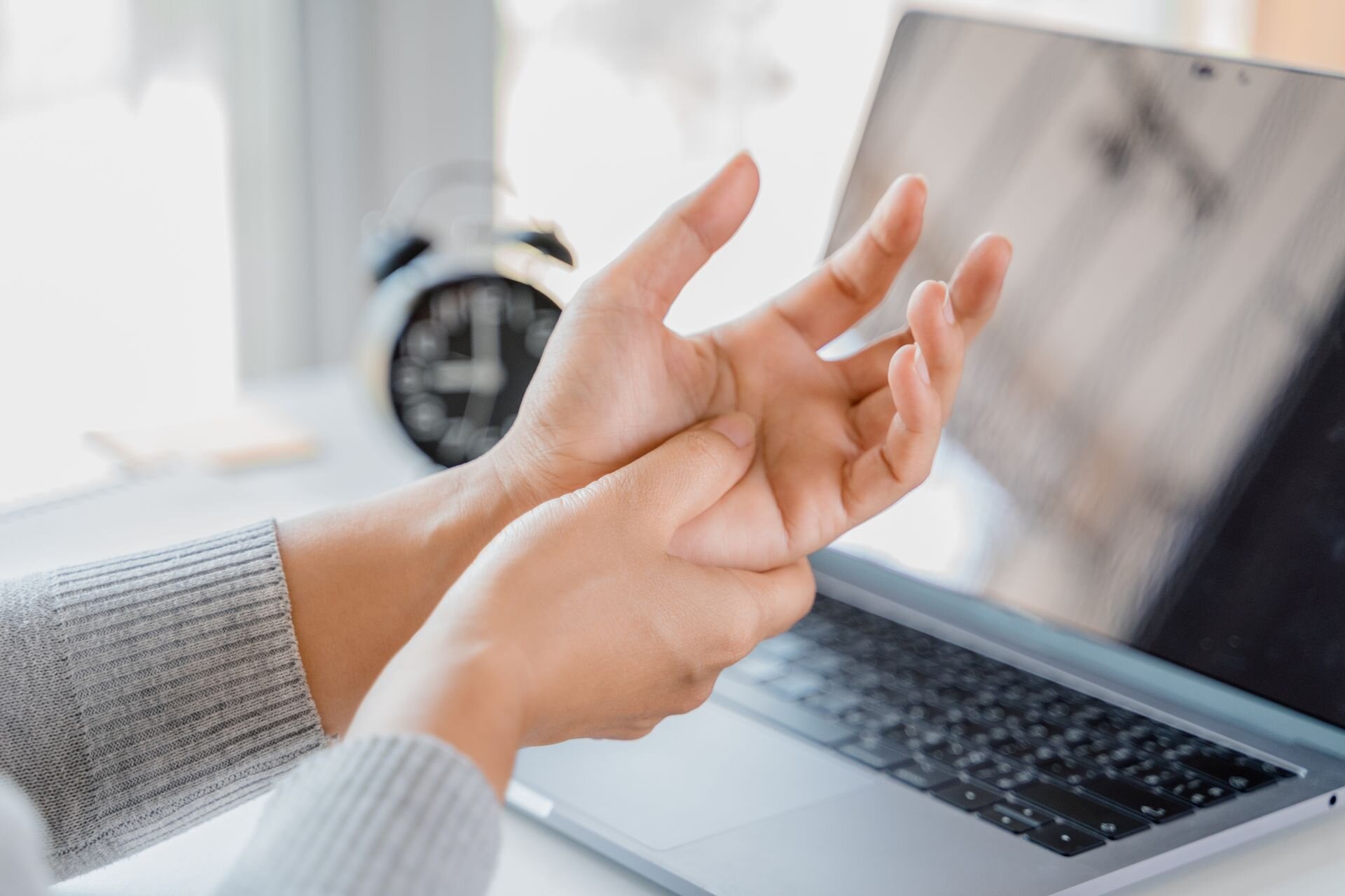 Frau hält sich schmerzhaft das Handgelenk beim Arbeiten am Laptop – typisches Symptom einer Sehnenscheidenentzündung.