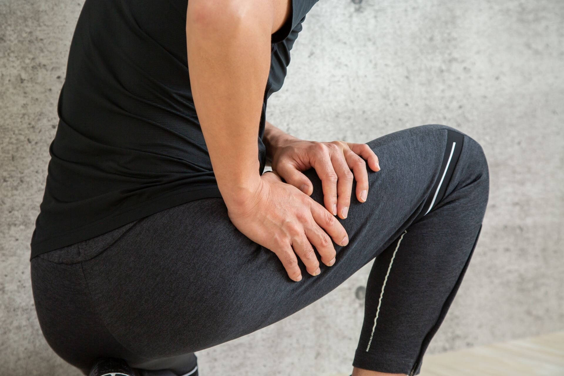 Mann mit Sportkleidung hält sich den Oberschenkel wegen Zerrung – typischer Schmerz bei Muskelverletzungen.